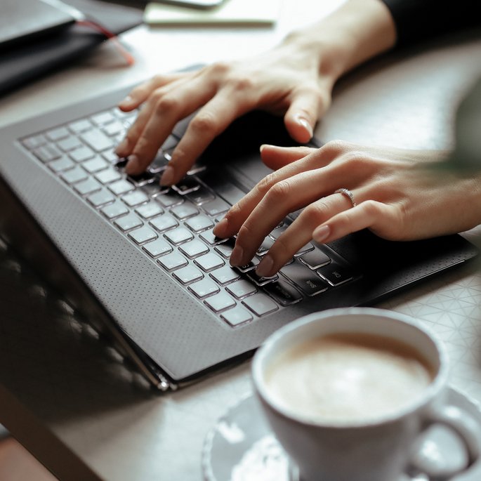 Kaffee und Laptop mit tippenden Händen darauf