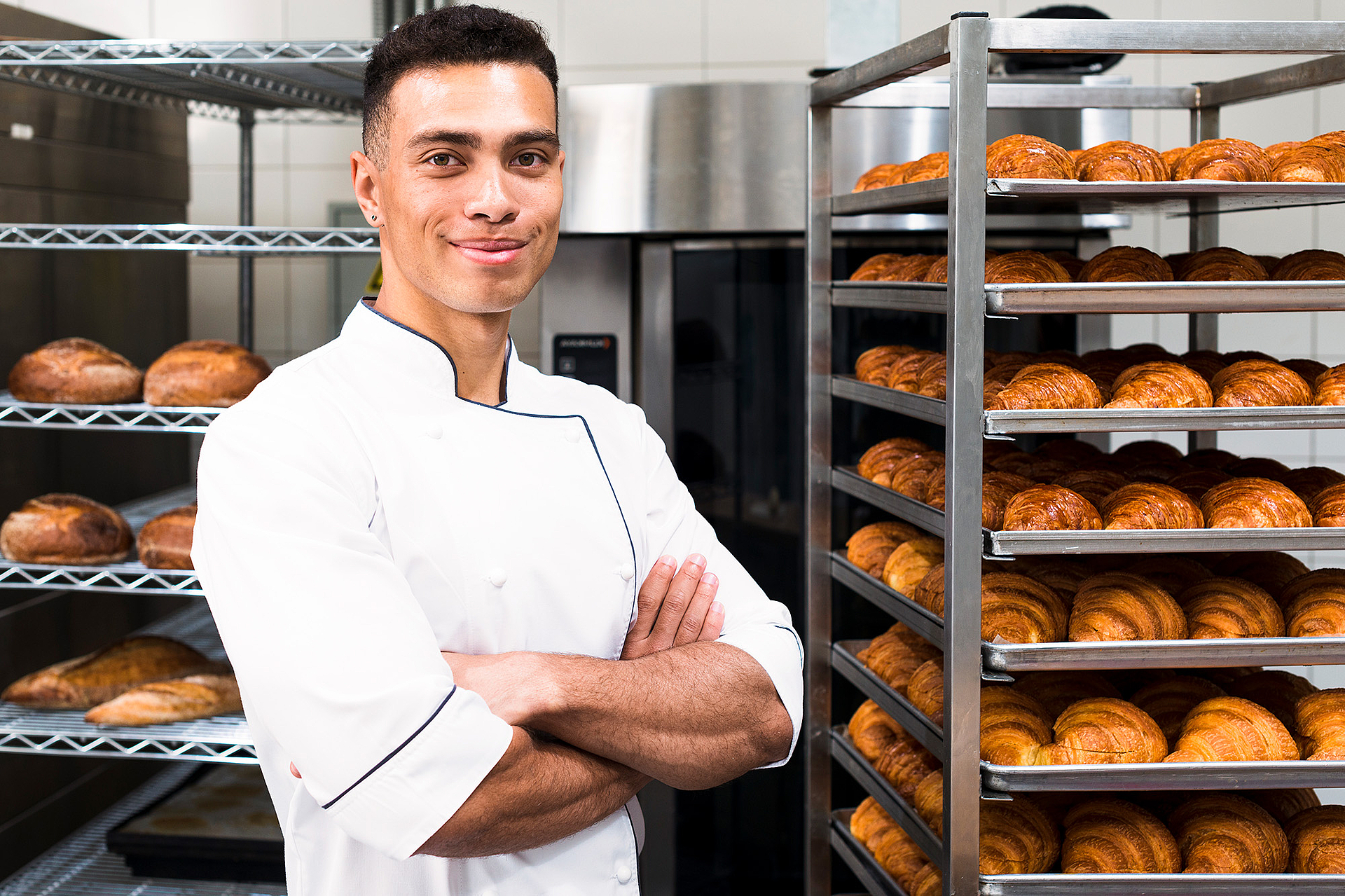 confident-young-male-baker-front-baked-croissant-shelves