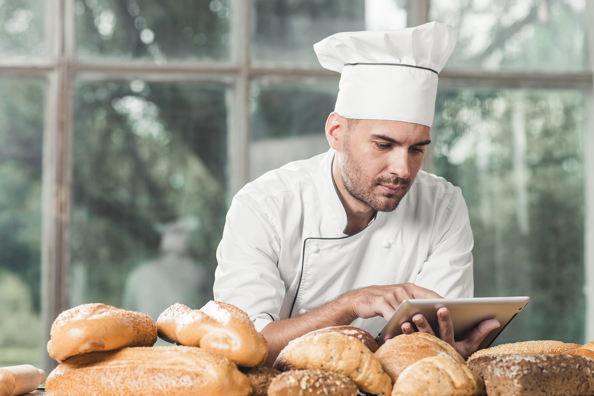 male-baker-using-digital-tablet-with-many-breads-table