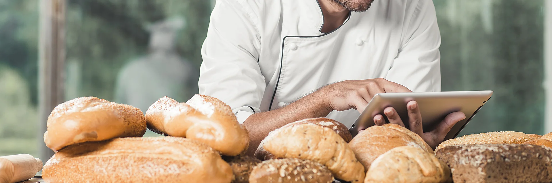 male-baker-using-digital-tablet-with-many-breads-table