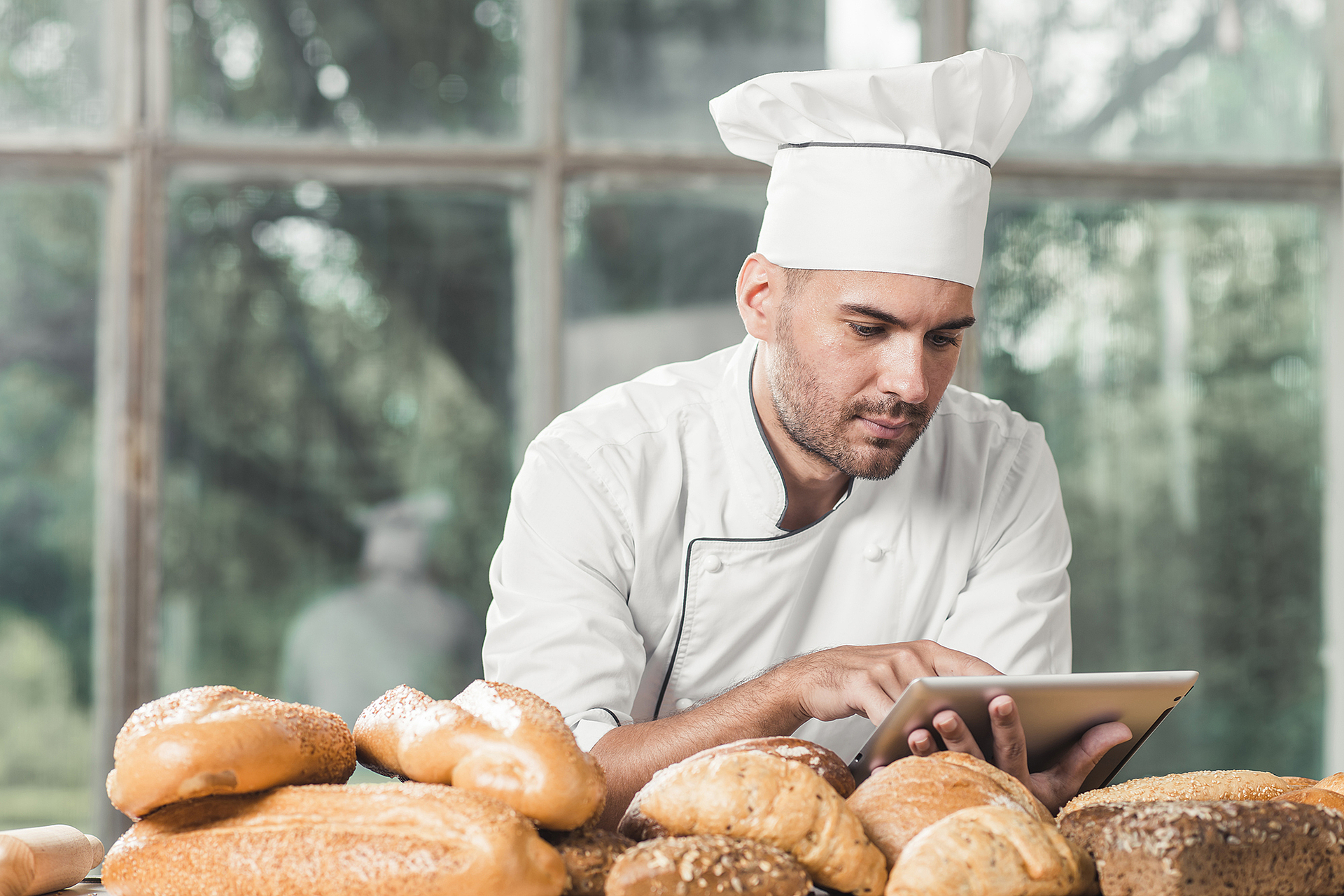 male-baker-using-digital-tablet-with-many-breads-table
